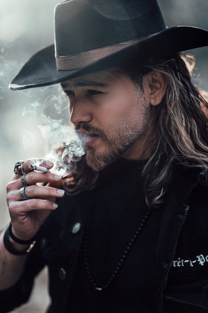 A man with a cowboy hat smoking, showcasing Western style and contemplation.