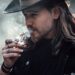 A man with a cowboy hat smoking, showcasing Western style and contemplation.